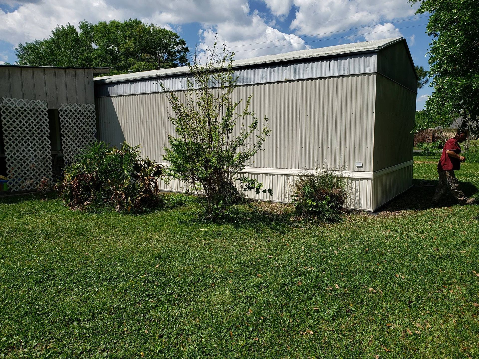 A man is standing in front of a shed in a grassy yard.