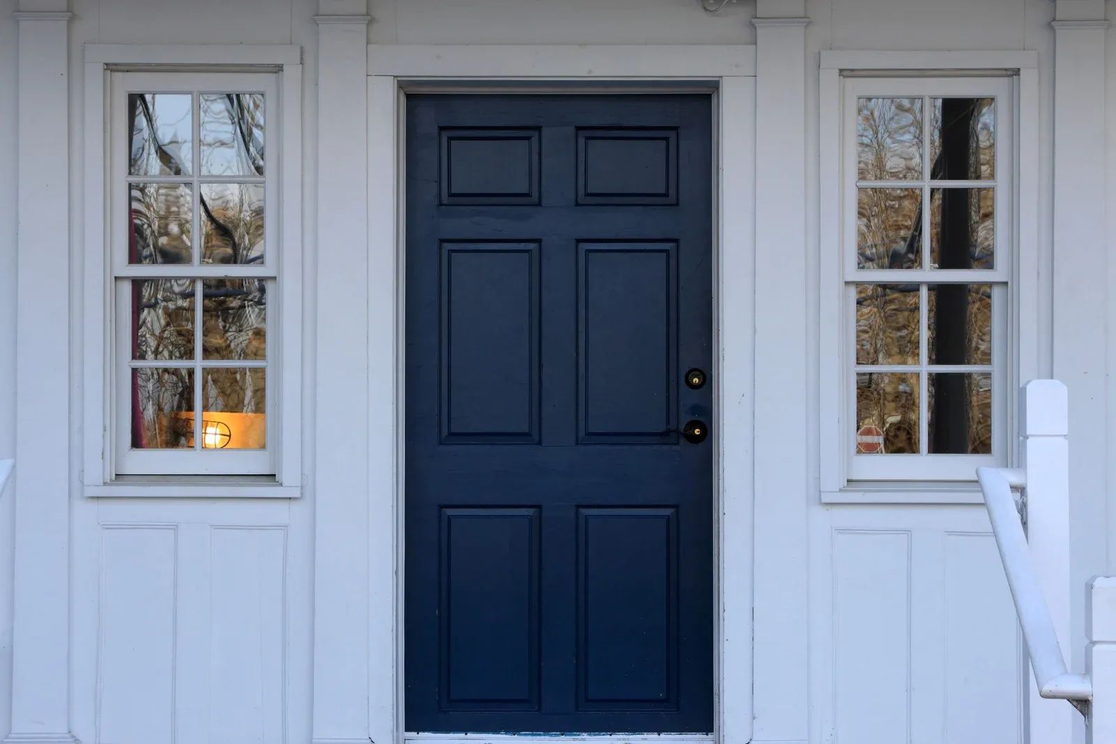 Blue door centered between two white-framed windows on a white house.