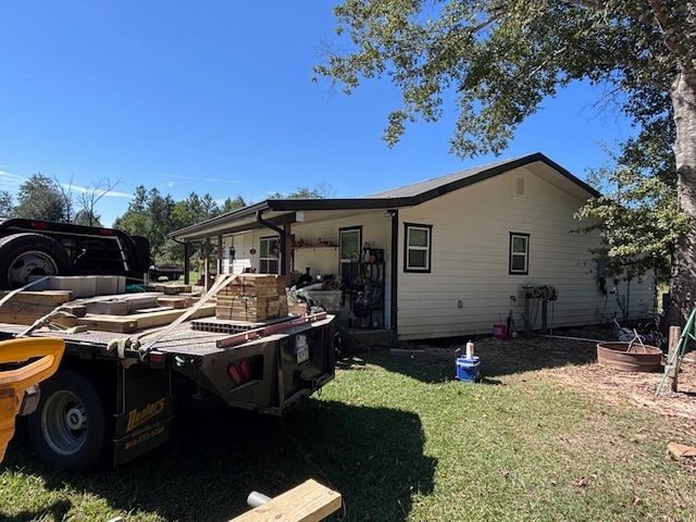 A white house with a black roof next to a flatbed truck on a sunny day.