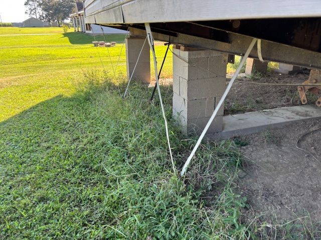 Gray cinder block supports a trailer, with white cables and tall grass in a grassy field.