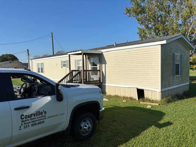 A beige mobile home with a small porch next to a work truck in a grassy yard.