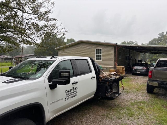 White work truck with company name, parked near a house with an open-sided shed. Cloudy sky.