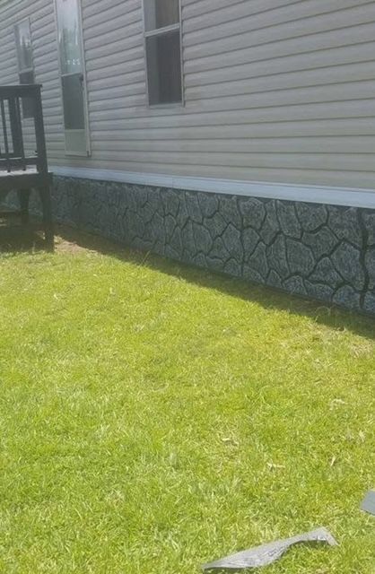 Side of a house with decorative stone skirting; green lawn in the foreground.