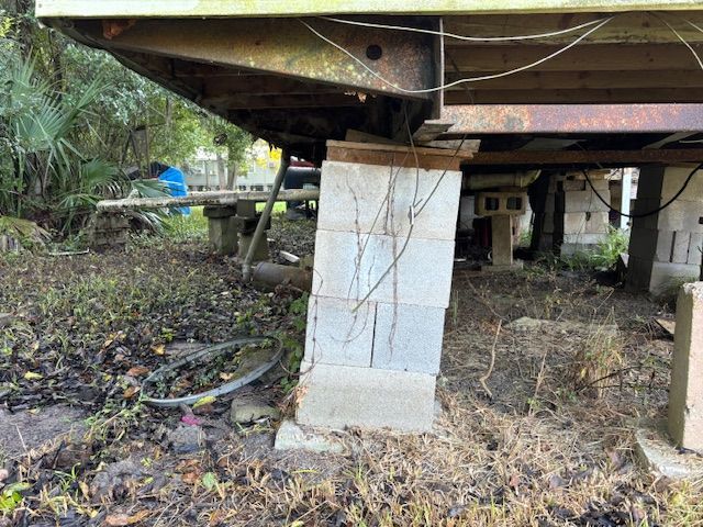 Leaning concrete block supporting a raised structure; overgrown vegetation surrounds.
