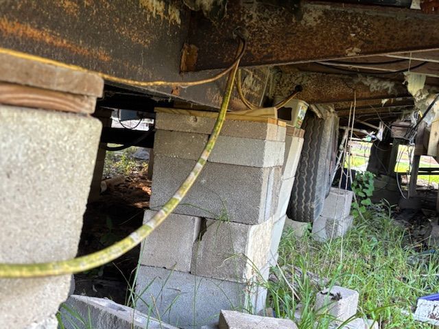 Mobile home supported by stacked cinder blocks, some leaning, outdoors with grass.