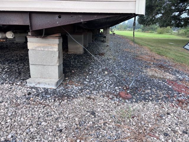 Mobile home supported by cinder blocks and anchored with a cable on a gravel foundation.