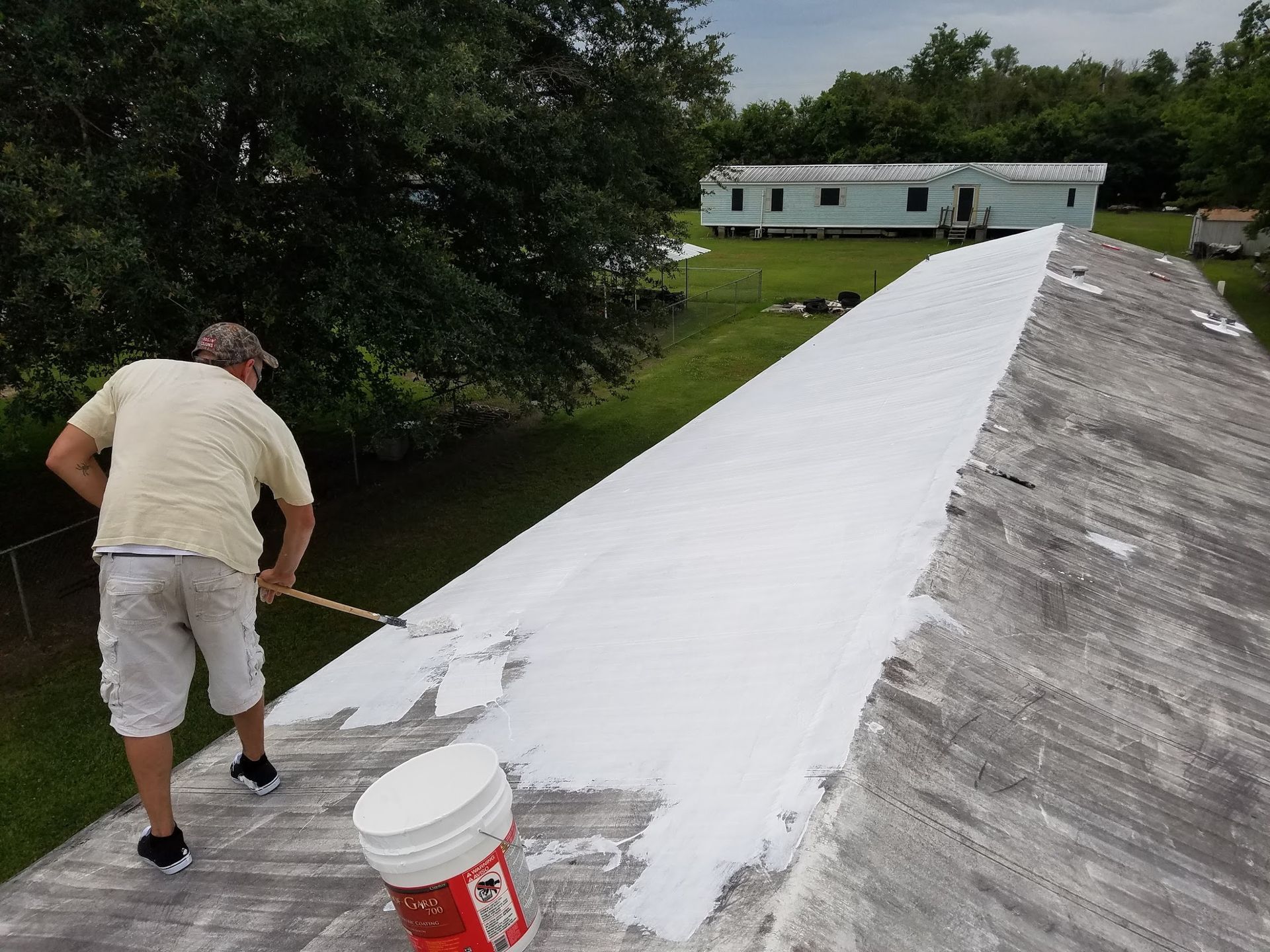 A man is painting a roof with white paint