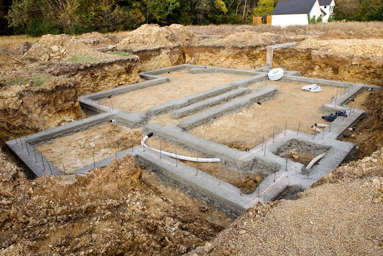Foundation of a house under construction, with concrete walls and dirt surrounding the excavated area.