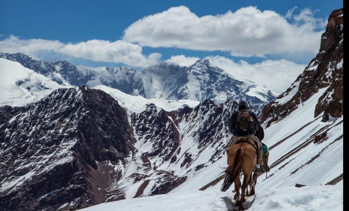 Dos personas a caballo recorriendo un sendero de montaña cubierto de nieve 