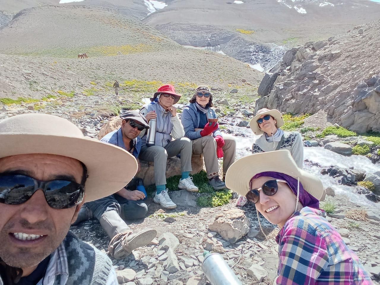 Grupo de personas descansando sobre rocas cerca de un arroyo en un paisaje montañoso.