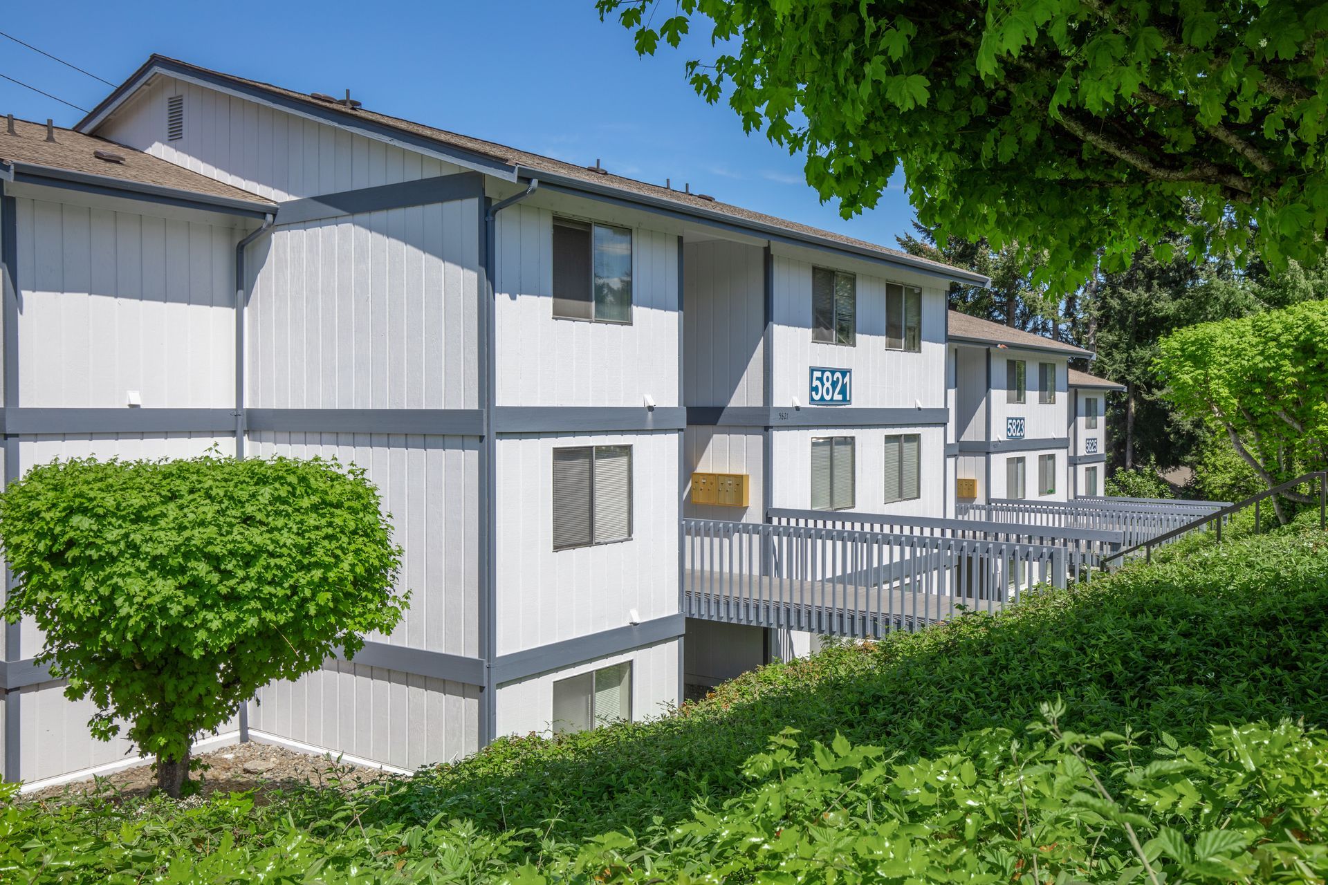 A white apartment building with a balcony and trees in front of it.