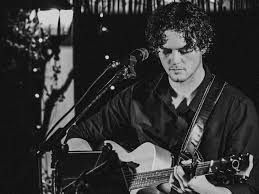 A man is sitting in a chair playing a guitar and singing into a microphone.