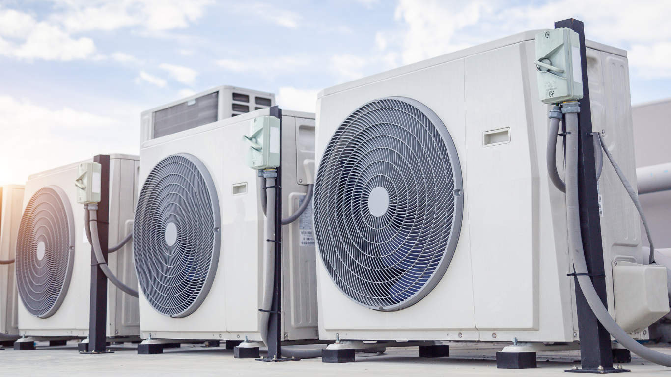 Air conditioning units on a rooftop, white with large fans, under a blue sky.