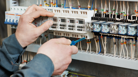 Hands of an electrician working on a control panel with wires and electronic components.
