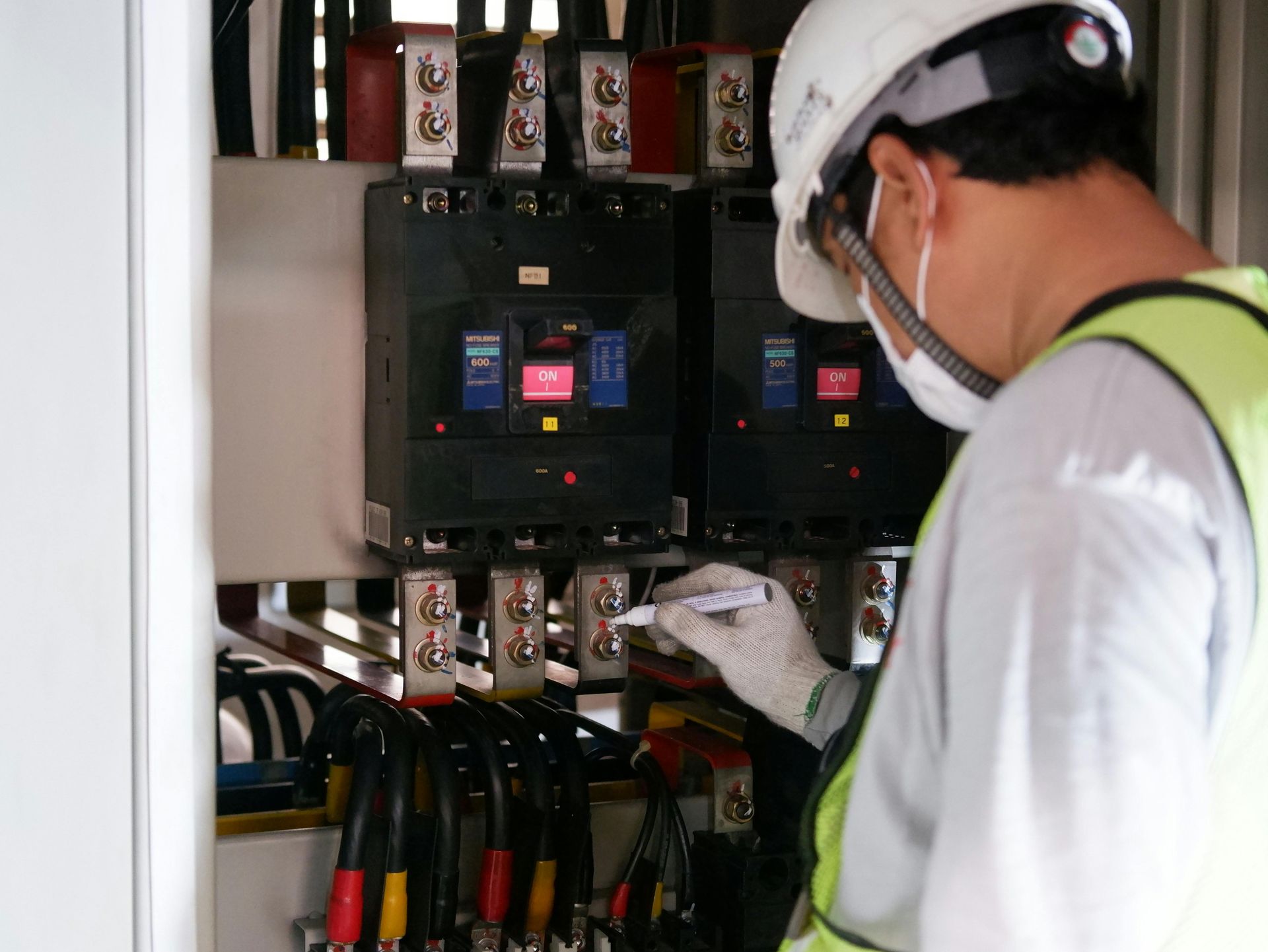 Technician in hard hat inspecting electrical control panel with exposed wiring in a utility room