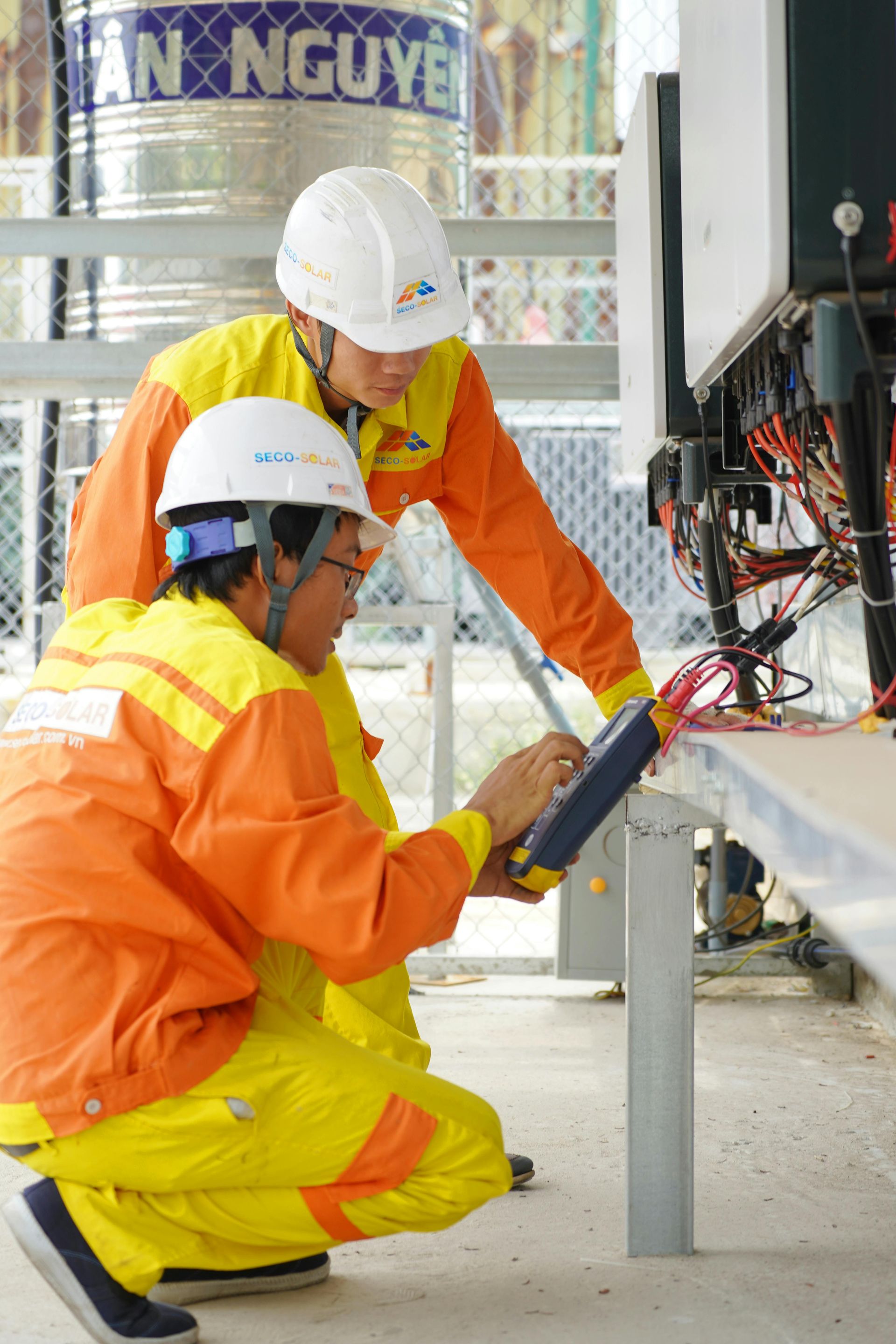 Two construction workers in orange safety gear inspecting electrical wiring at a worksite