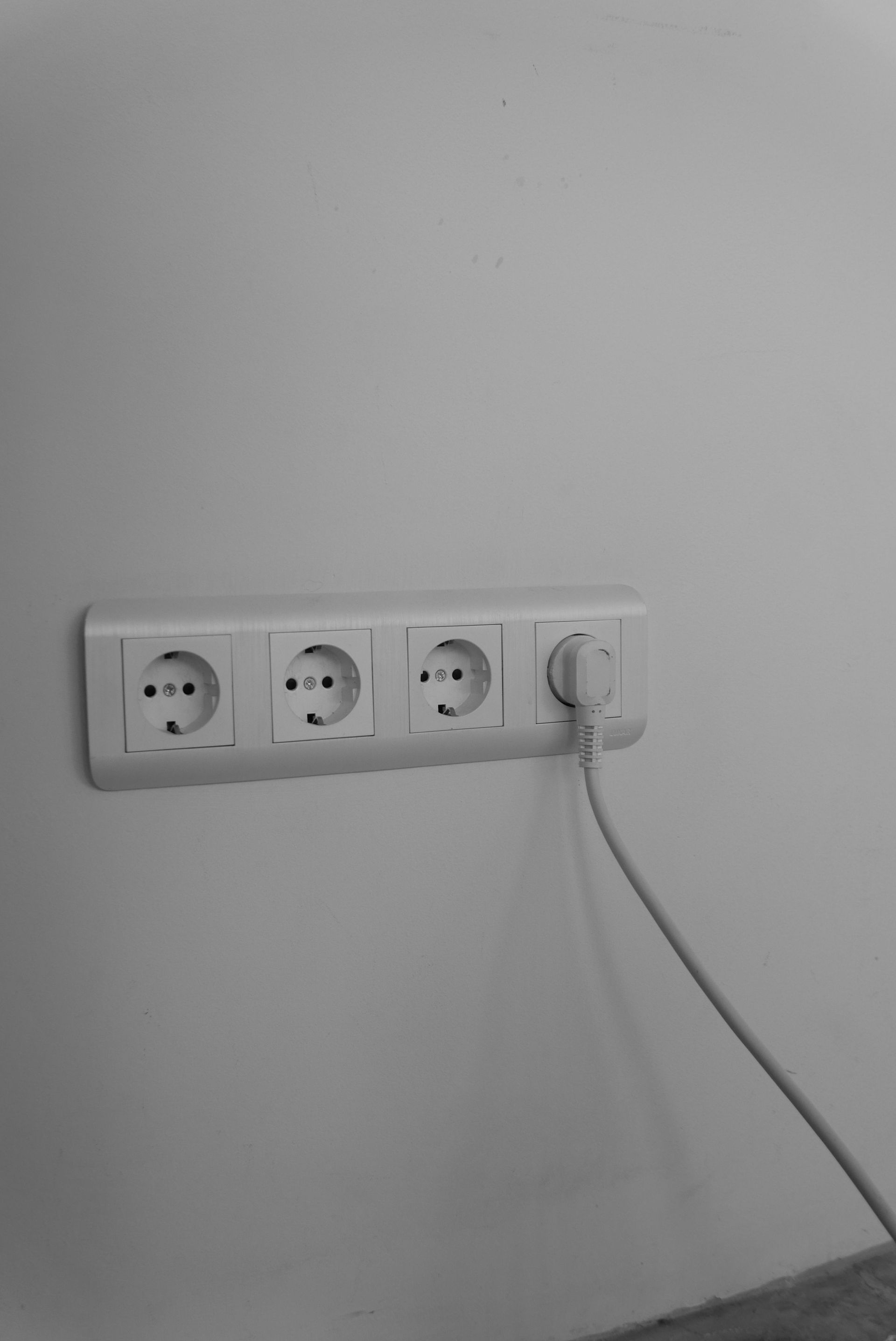 Wall outlet strip on a gray wall with one plug and cord connected