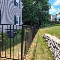 A metal fence is surrounding a stone wall in front of a house.