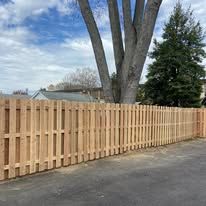 A wooden fence is sitting next to a tree in a parking lot.
