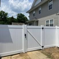 A white vinyl fence with a gate in front of a house.