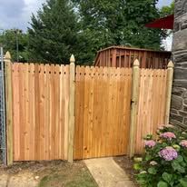 A wooden fence with a gate in front of a stone building.