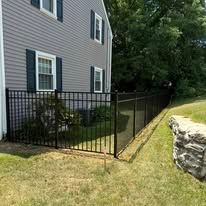 A black metal fence surrounds a lush green yard in front of a house.