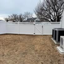 A backyard with a white fence and two air conditioners.
