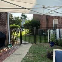 A gazebo is sitting in front of a brick house next to a fence.