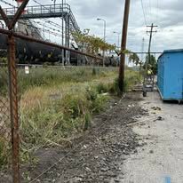 A blue dumpster is parked next to a chain link fence.
