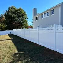 A white vinyl fence surrounds a lush green yard in front of a house.