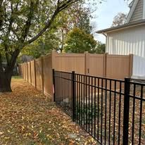 A wooden fence with a black metal fence in front of a house.