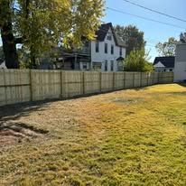 A wooden fence surrounds a lush green field in front of a house.