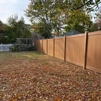 A wooden fence surrounds a yard filled with leaves.