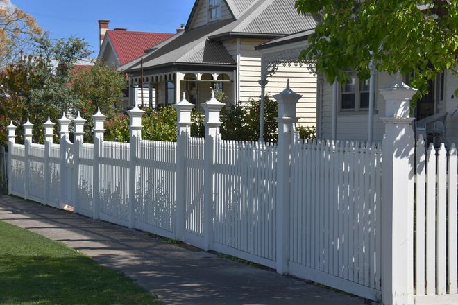 A white picket fence surrounds a house on a sunny day.