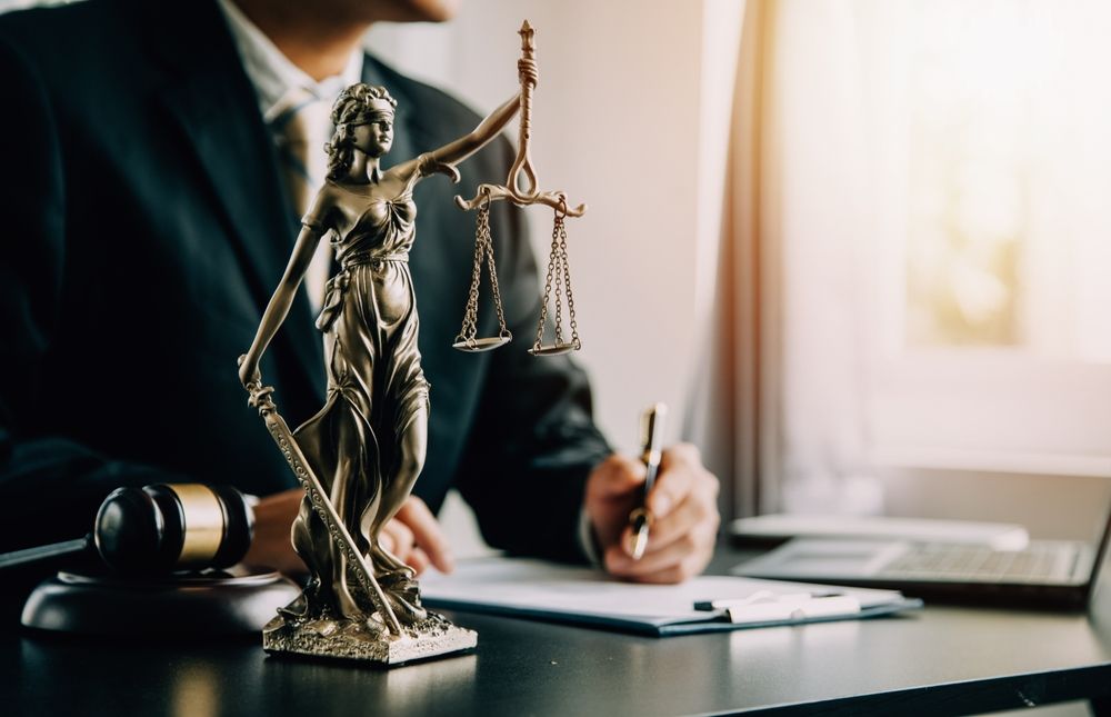 A man in a suit is sitting at a desk with a statue of justice.