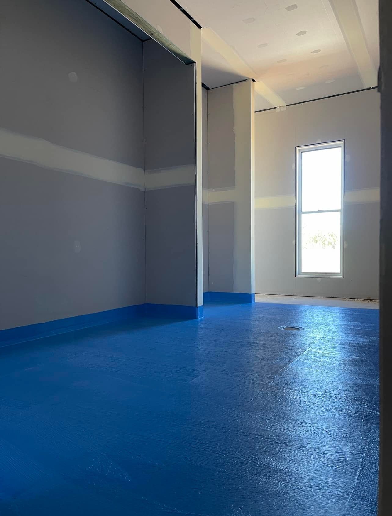 An Empty Room with a Blue Floor And a Window — Waterproofing Solutions in Toowoomba, QLD