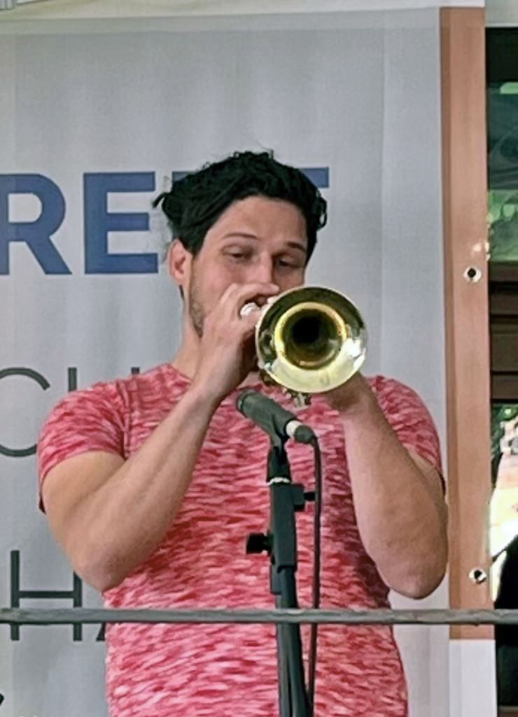 Ein Mann in einem roten Hemd spielt vor einem Mikrofon Trompete.