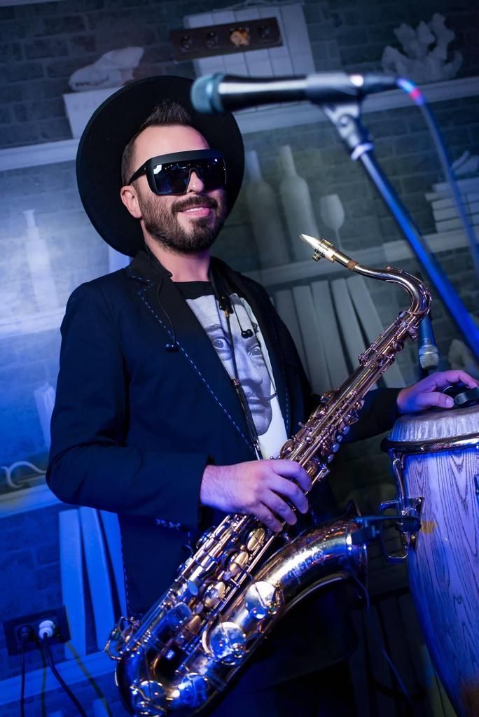 Ein Mann mit Hut spielt vor einem Mikrofon Saxophon.