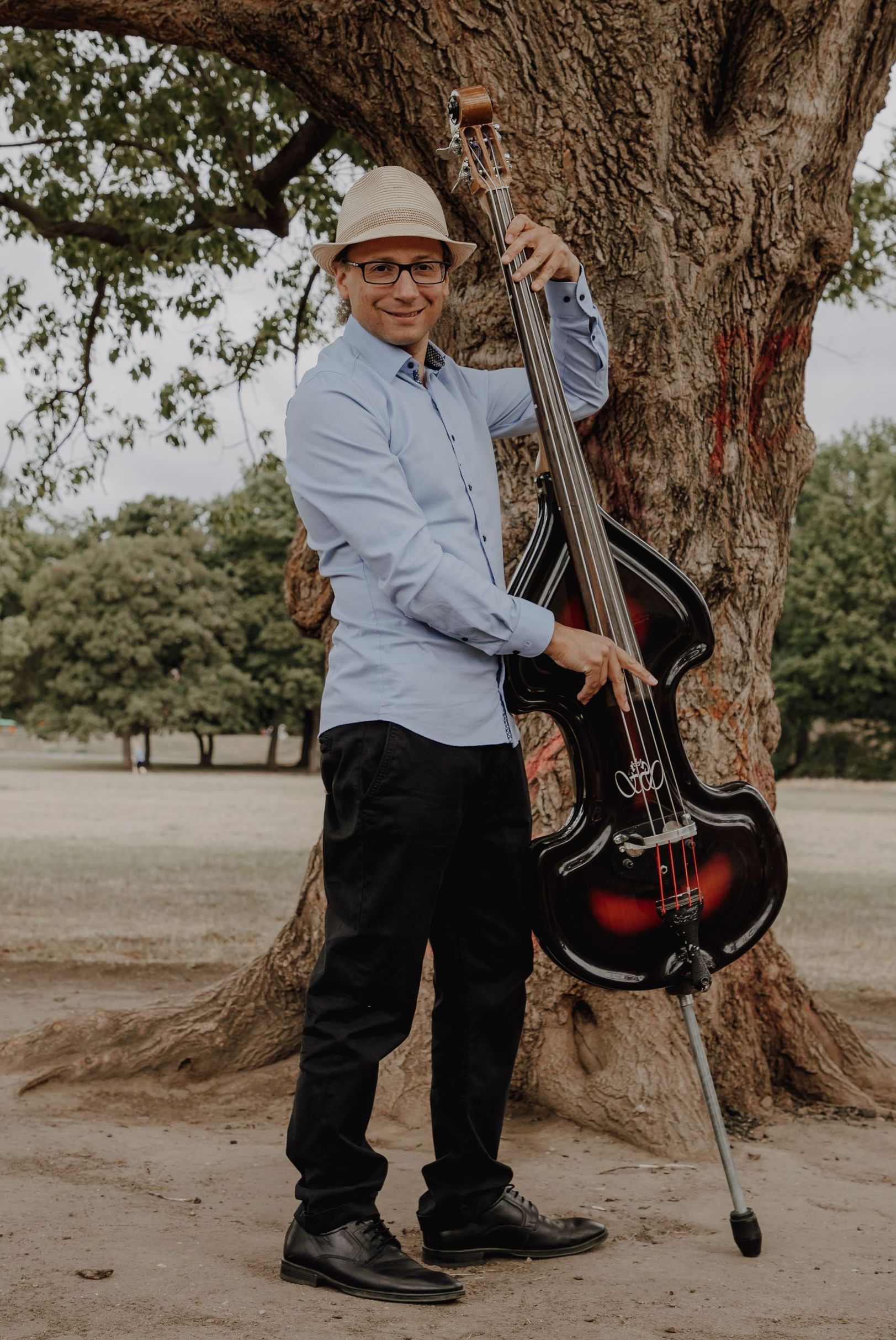 Ein Mann steht mit einer Gitarre in der Hand neben einem Baum.