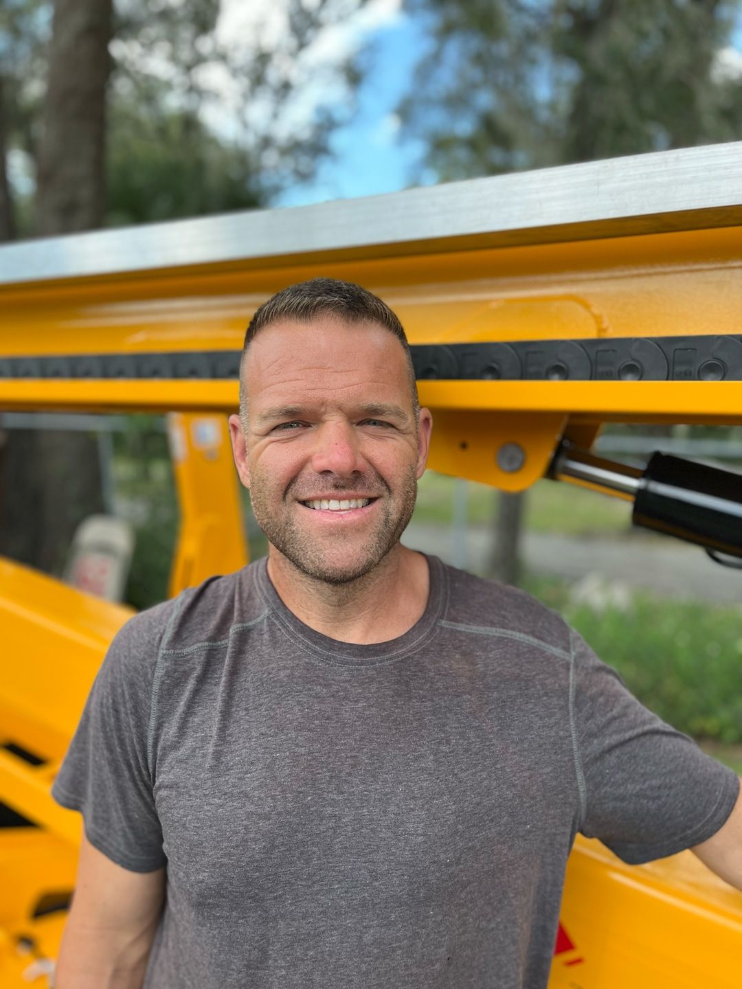 A man is standing in front of a yellow vehicle and smiling.