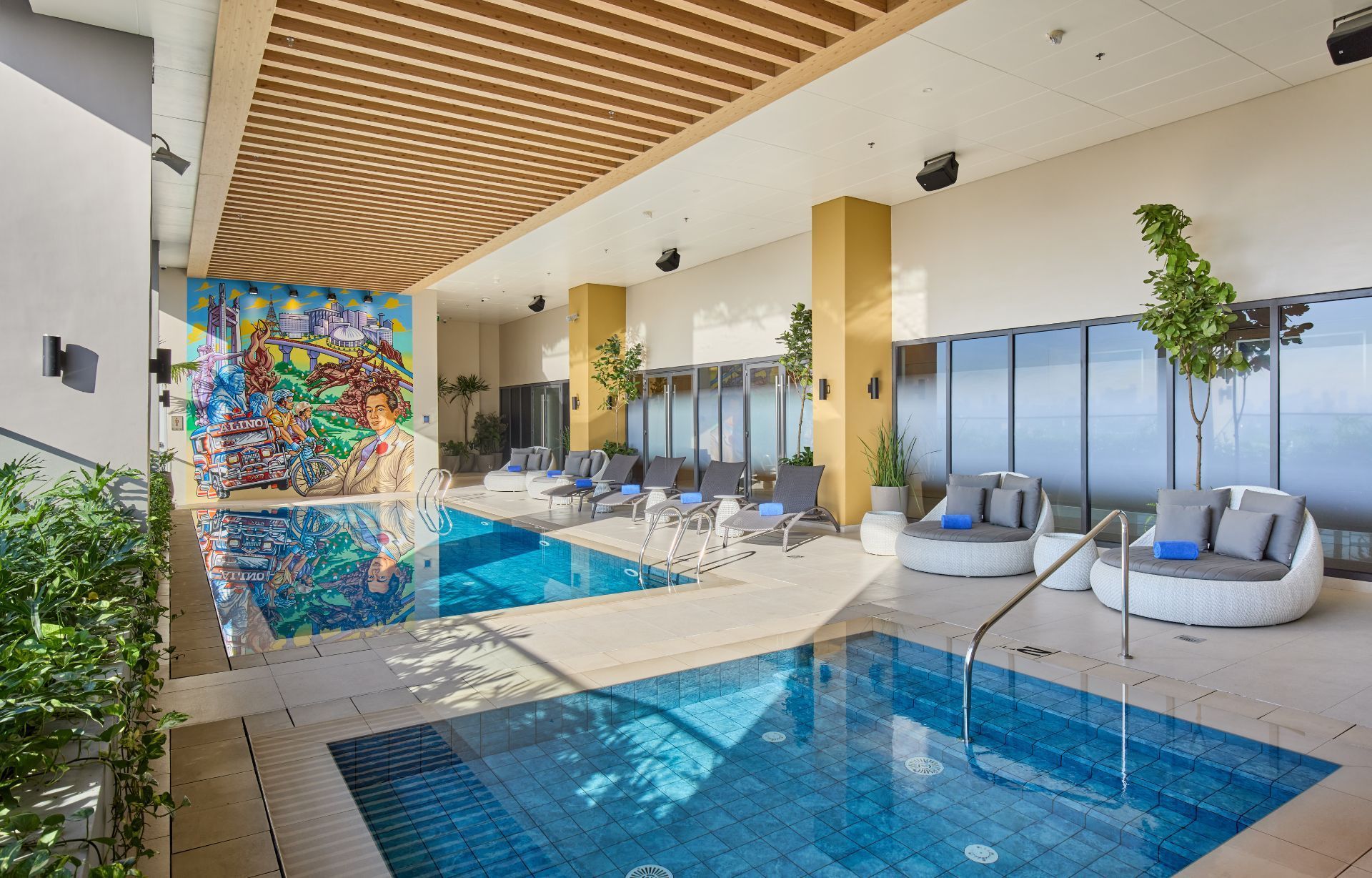 Indoor pool with lounge chairs, plants, and large window.
