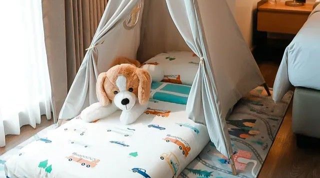 A cozy indoor teepee tent set up on a rug with a plush beagle toy resting on a vehicle-patterned mattress.