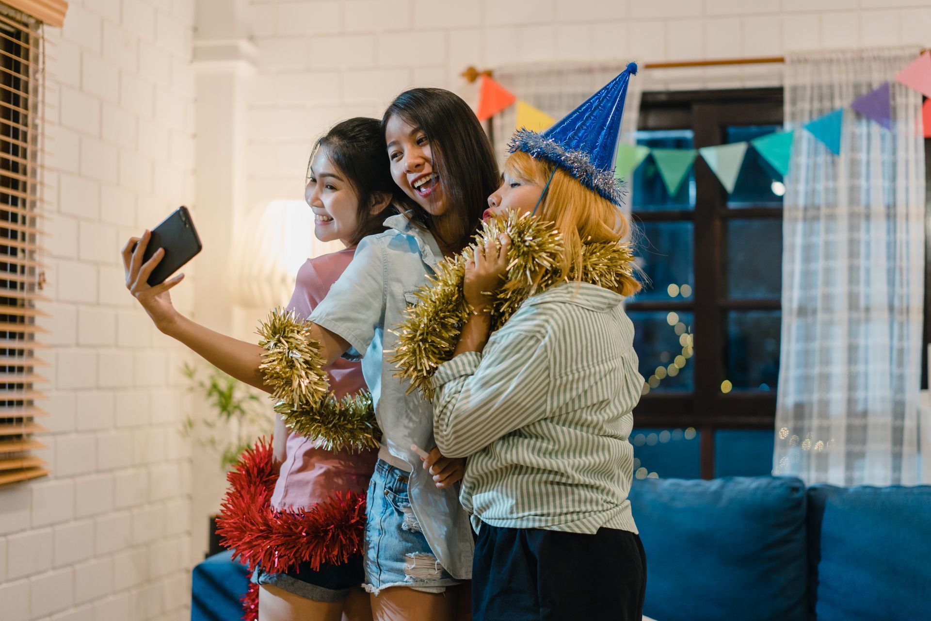Three people taking a selfie at a party, one with a party hat and tinsel.