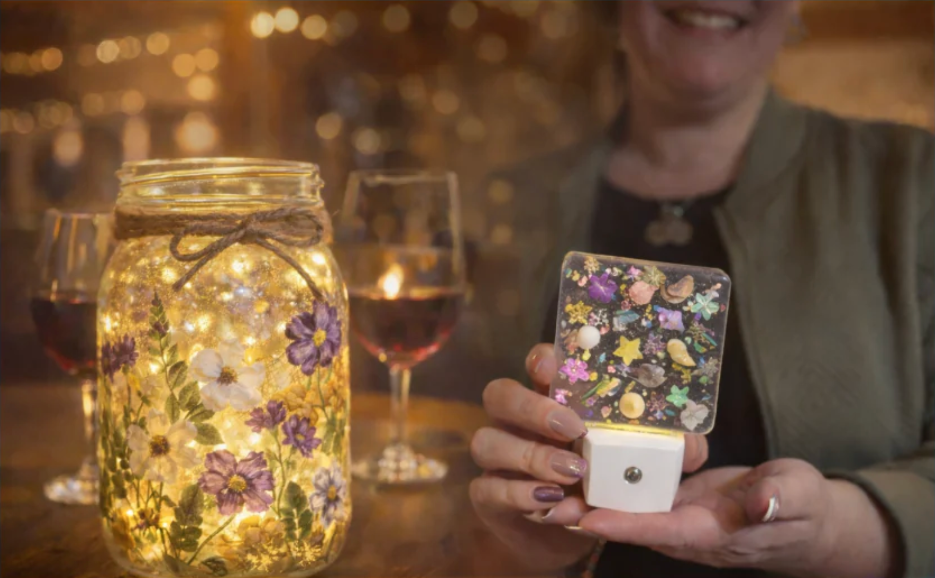 Woman holding a decorative nightlight next to a mason jar lit with fairy lights and dried flowers.