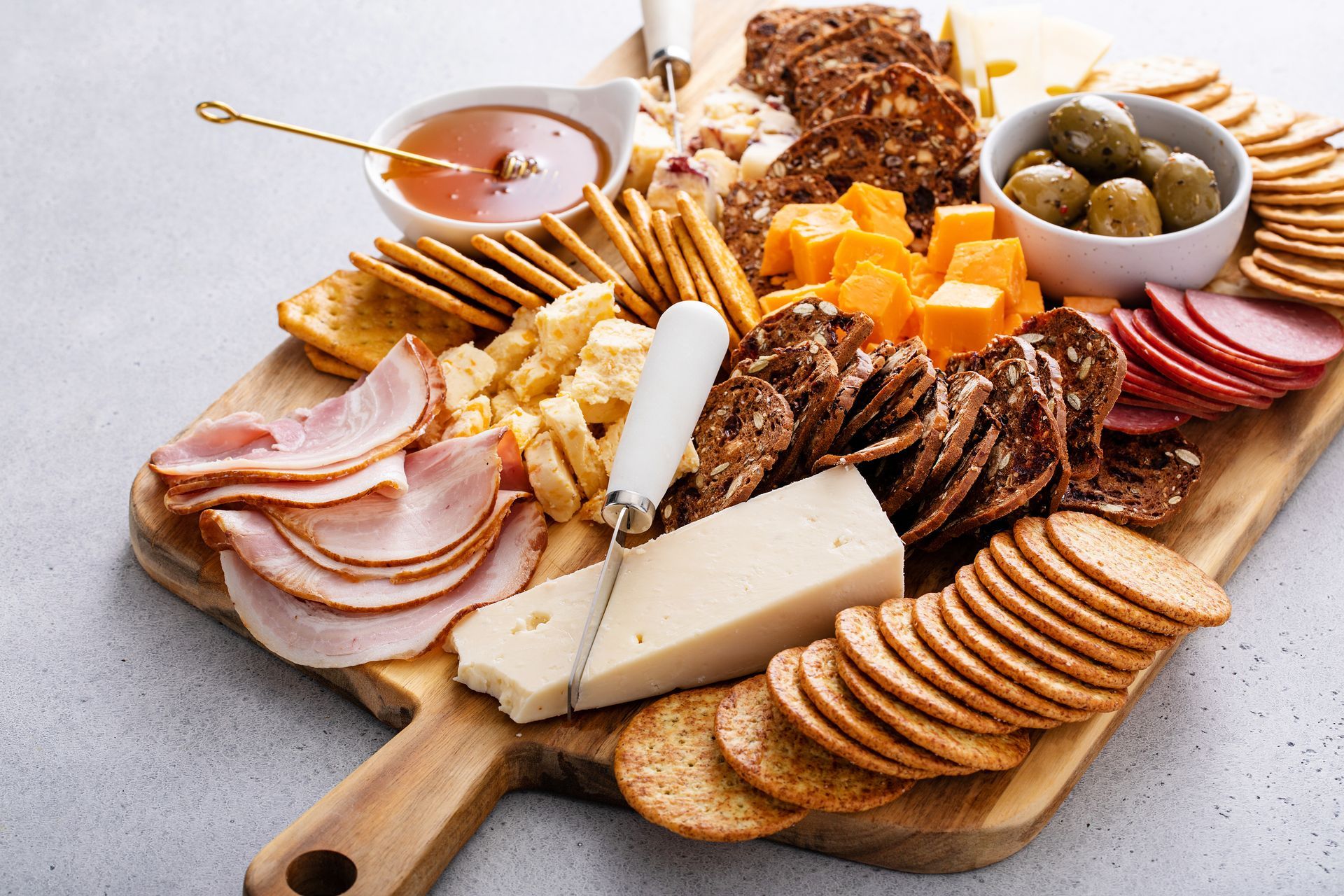 A wooden cutting board topped with crackers , cheese , ham and olives.