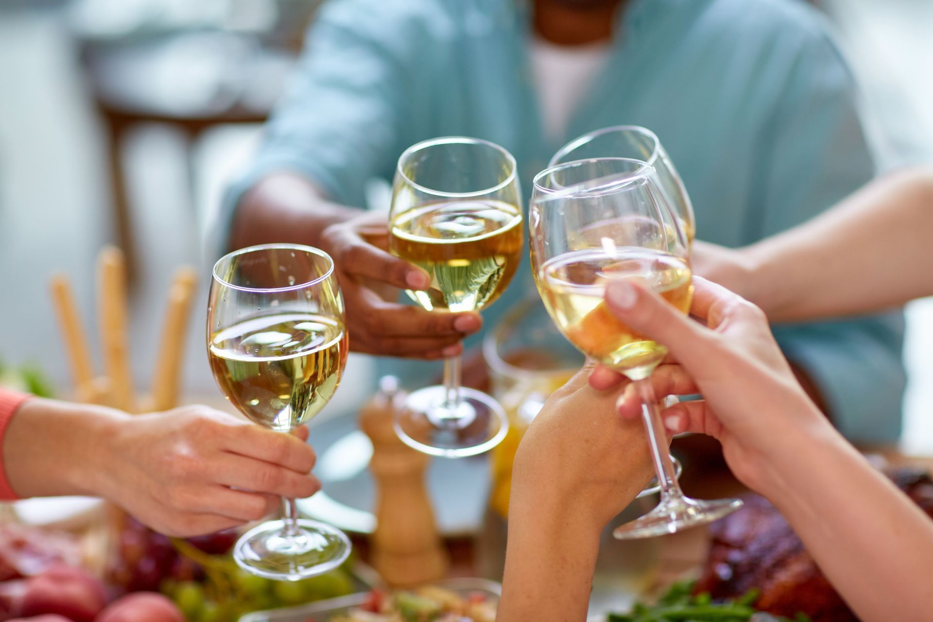 Hands clinking wine glasses in a toast, gathered around a dining table with food.