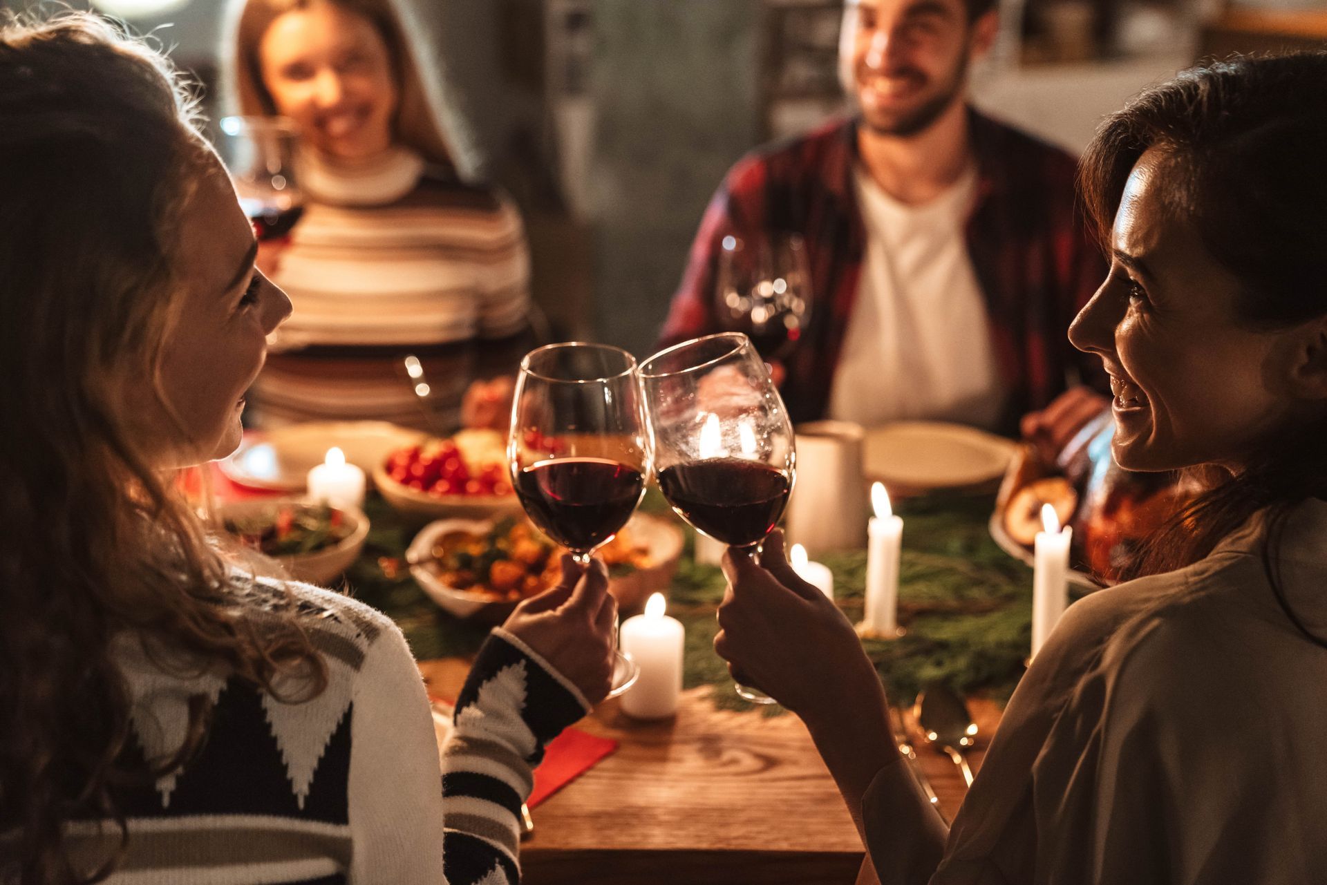 People toasting with wine glasses around a dinner table with food and candles.