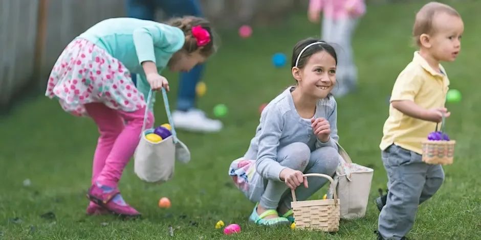 Three children gather colorful plastic eggs in a grassy yard during an Easter egg hunt.