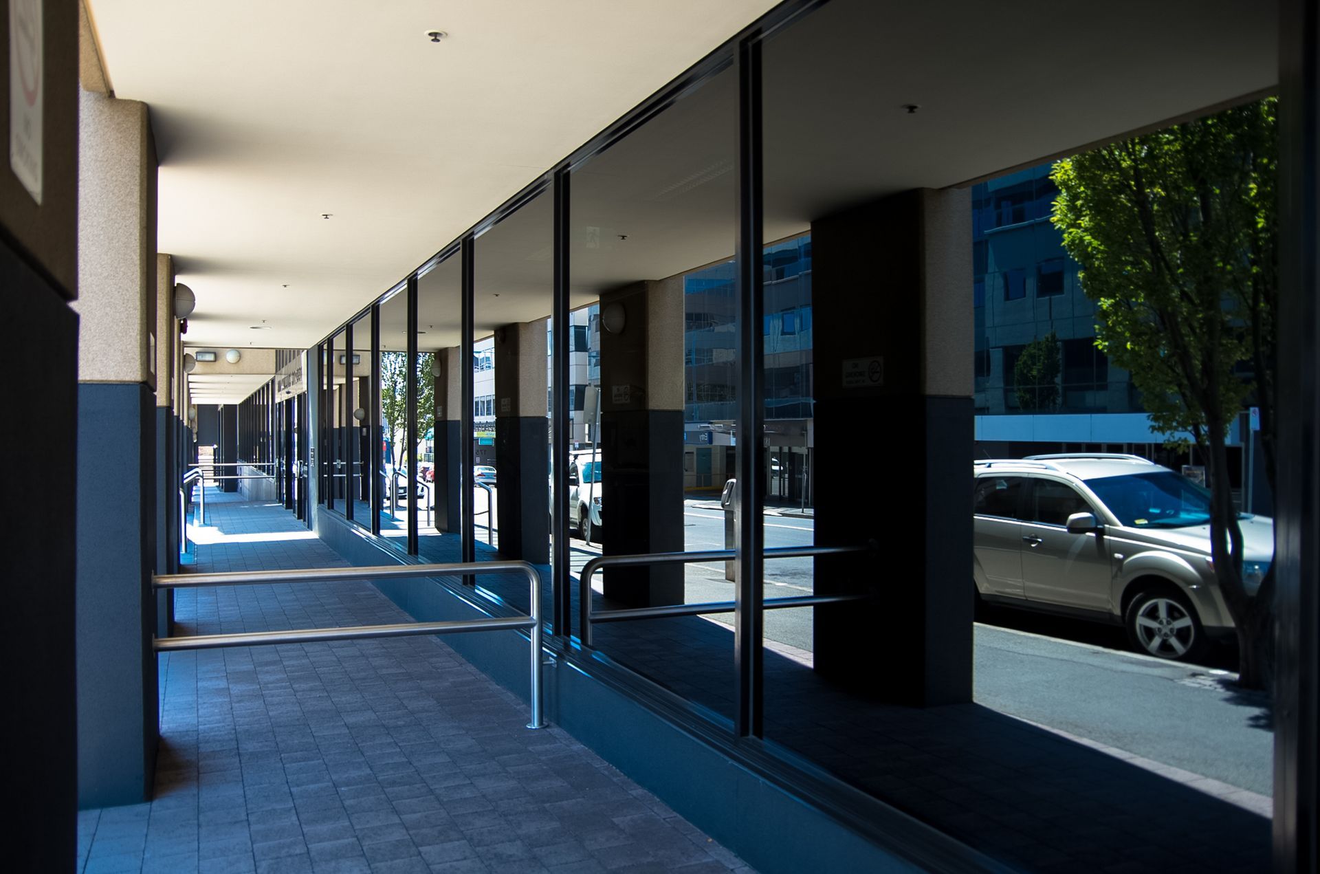 Covered sidewalk with glass storefront windows and parked cars reflected in the glass
