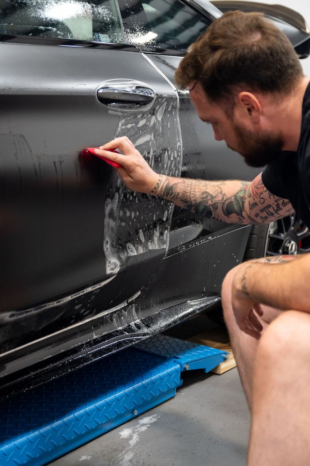 Man scrubbing a black car door with a sponge in a garage-like setting